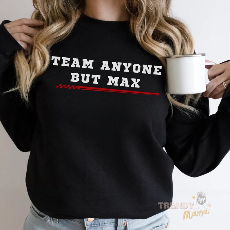 Peut inclure: Sweat-shirt noir avec un texte blanc qui dit "Team Anyone But Max" avec une ligne rouge &agrave; damier en dessous.