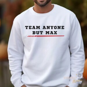 Peut inclure: Sweat-shirt blanc avec le texte "TEAM ANYONE BUT MAX" en lettres noires avec une bande rouge en dessous.