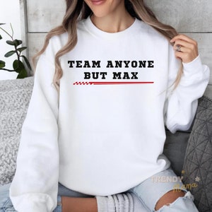 Peut inclure: Sweat-shirt blanc avec un texte noir qui dit "Team Anyone But Max" avec une ligne rouge &agrave; carreaux en dessous.