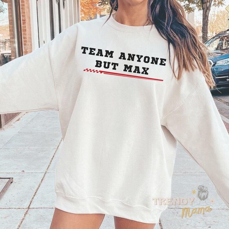 Peut inclure: Sweat-shirt blanc avec le texte "Team Anyone But Max" en lettres noires avec une ligne rouge &agrave; carreaux en dessous.