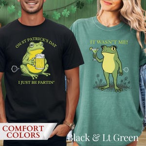 Peut inclure: T-shirts noirs et vert clair avec des motifs de grenouilles. Le t-shirt noir présente une grenouille tenant une bière et le texte "ON ST PATRICK'S DAY I JUST BE FARTIN'". Le t-shirt vert clair montre une grenouille avec un martini et le texte "IT WASN'T ME!".