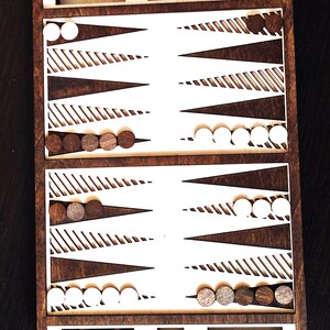 May include: A wooden backgammon board game set with white and brown pieces. The board has a brown background with white triangles and stripes. The pieces are arranged on the board in a game in progress.
