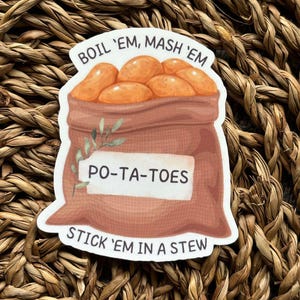 Peut inclure: Un sac en toile de jute brun avec une étiquette blanche qui indique "PO-TA-TOES". Le sac est rempli de pommes de terre orange et porte le texte "BOIL 'EM, MASH 'EM" au-dessus du sac et "STICK 'EM IN A STEW" en dessous du sac.