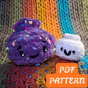 May include: A large purple crocheted plush with colorful flecks and a smaller white crocheted plush, both featuring black embroidered eyes and mouths. An orange rectangular graphic with the white text PDF PATTERN is overlaid on the image.