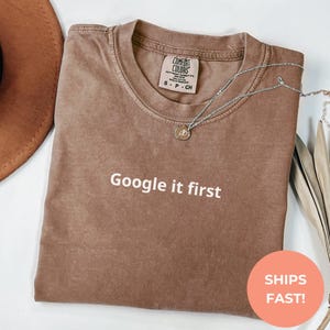 May include: A brown t-shirt with the text "Google it first" printed in white on the front.