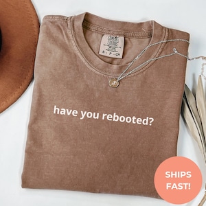 Peut inclure: Un t-shirt marron avec le texte "have you rebooted?" imprimé en blanc.