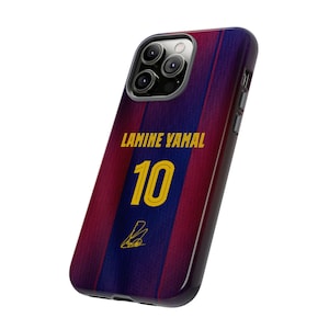 以下が含まれることがあります： サッカーのユニフォームにインスパイアされたデザインの携帯電話ケース。赤と青のストライプ模様で、「LAMINE YAMAL」という名前と「10」の数字が金色で表示されています。サインも確認できます。