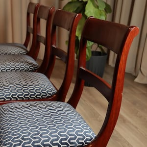 Könnte beinhalten: Vier Esszimmerstühle aus Holz mit dunkelbraunen Holzrahmen und Sitzflächen aus blau-weiß gemustertem Stoff.