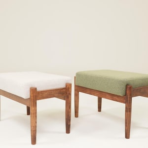 May include: Two mid-century modern ottomans. One has a white, textured cushion, and the other has a green cushion. Both have wooden frames and four legs. The ottomans are rectangular and appear to be made of wood and fabric.