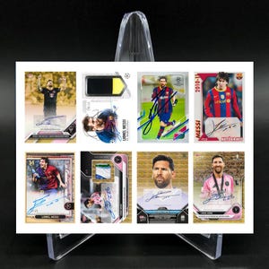 Puede incluir: Una colección de ocho cromos de Lionel Messi, cada uno con una imagen diferente del futbolista. Las tarjetas muestran a Messi con varios uniformes y poses de equipo, algunas con su autógrafo. Las tarjetas se exhiben en un soporte transparente sobre un fondo negro.