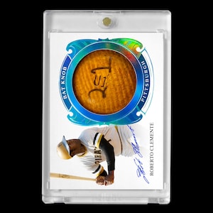May include: A baseball card encased in a clear protective holder. The card features a bat knob with the text "U1" and "BAT KNOB PITTSBURGH". Below is a photo of Roberto Clemente in a Pirates uniform, with his signature.