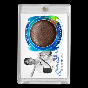May include: A baseball card featuring a brown bat knob, the text "BAT KNOB" and "NY YANKEES", and a black and white image of Mickey Mantle. The card is encased in a clear plastic holder.