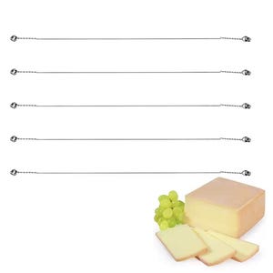 Könnte beinhalten: Fünf Käseschneider mit Drahtklingen, zusammen mit einem Käseblock, Käsescheiben und grünen Trauben. Der Käse hat eine hellgelbe Farbe, der Hintergrund ist weiß.