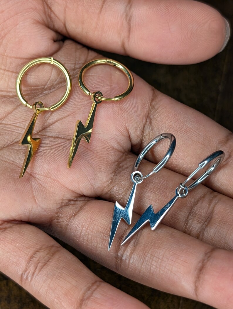 Pode incluir: Dois pares de brincos com um charme de raio. Um par &eacute; dourado e o outro &eacute; prateado.