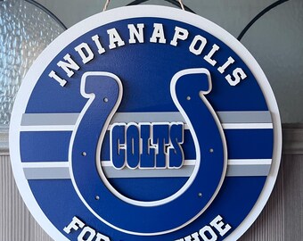 Könnte beinhalten: Rundes Holzschild in Blau und Weiß mit dem Schriftzug "Indianapolis Colts" in Weiß. Das Schild zeigt das Colts-Logo, ein Hufeisen, und den Schriftzug "For The Shoe". Das Schild hängt an einer Tür.
