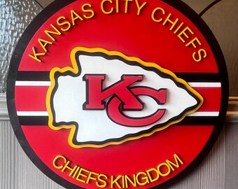 Könnte beinhalten: Ein rundes Holzschild mit rotem Hintergrund und schwarzem Rand. Das Schild zeigt das Logo der Kansas City Chiefs in Weiß, Rot und Gelb mit dem Text "Kansas City Chiefs" in Gelb oben herum und "Chiefs Kingdom" in Gelb unten herum.