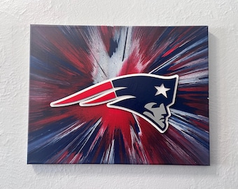 Könnte beinhalten: Ein Leinwandkunstwerk mit dem Logo der New England Patriots. Das Logo ist weiß umrandet, mit einem marineblauen Kopf und einem rot-weißen Streifen. Der Hintergrund hat ein radiales Burst-Design in Rot, Weiß und Blau.