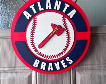Könnte beinhalten: Ein rundes Holzschild in Rot, Weiß und Blau mit den Worten "Atlanta Braves" und einem Baseball mit einer Tomahawk.