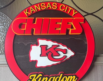 Könnte beinhalten: Ein rotes, weißes und schwarzes Holzschild mit den Worten "Kansas City Chiefs Kingdom" in gelber Schrift. Das Schild zeigt das Logo der Kansas City Chiefs mit einem weißen Pfeilspitz und den Buchstaben "KC" in rot.
