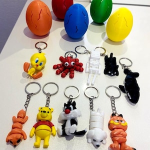 May include: A selection of keyrings featuring cartoon characters and colourful egg-shaped objects. The keyrings include characters like Tweety Bird, Winnie the Pooh, Sylvester the Cat, and Garfield. The eggs are orange, red, blue, green, and yellow.