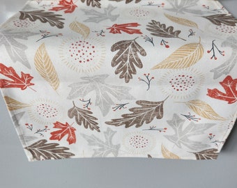 May include: A white table runner featuring a fall leaf design. The leaves are in shades of brown, red, and gold. There are also small red berries and white dots on the runner.