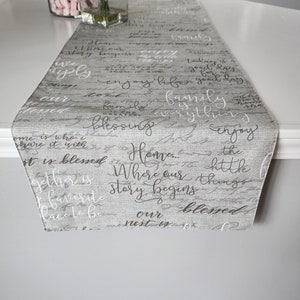 May include: A gray and white table runner with a handwritten design featuring the words "Home... Where our story begins" and "Blessed."