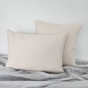 May include: Two cream-colored fluffy throw pillows on a white and gray textured fabric.