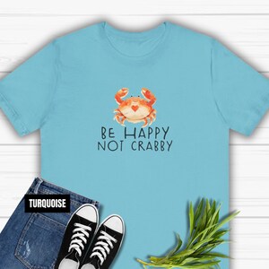 May include: A turquoise blue t-shirt with a cartoon crab and the text "Be Happy Not Crabby".