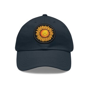May include: A navy blue baseball cap with a smiling sunflower patch. The sunflower is yellow and orange with a black outline.