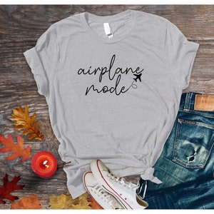 Puede incluir: Una camiseta gris con el texto "airplane mode" en letra negra con un peque&ntilde;o icono de avi&oacute;n y una l&iacute;nea punteada.