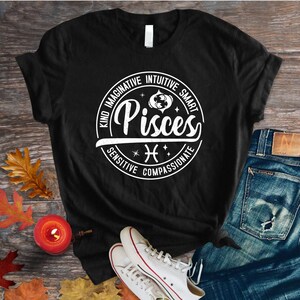 Może przedstawiać: Czarny T-shirt z białym kołem graficznym przedstawiającym znak zodiaku Ryby. Grafika koła zawiera słowa "Kind, Imaginative, Intuitive, Smart, Sensitive, Compassionate".