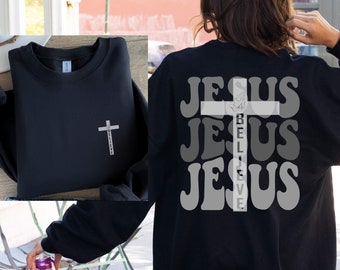 Peut inclure: Sweat-shirt noir avec une croix blanche et les mots "Believe" et "Jesus" imprimés sur le devant et le dos. Le dos présente le mot "Jesus" répété trois fois avec une croix blanche au milieu.