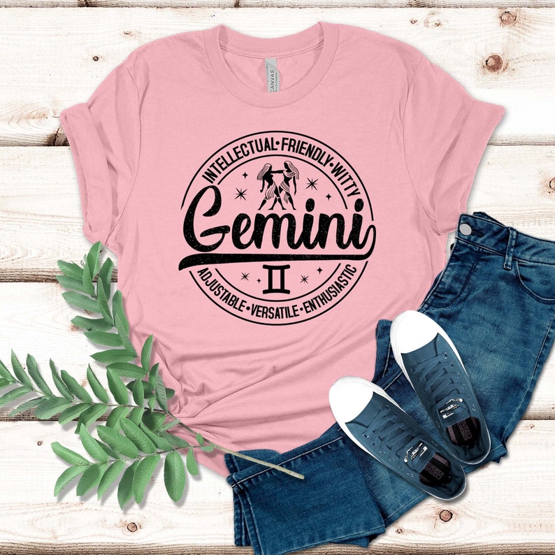 May include: Pink t-shirt with a black circle graphic featuring the Gemini zodiac sign and the text "Gemini II" with the words "Intellectual - Friendly - Witty - Adjustable - Versatile - Enthusiastic" around the circle.