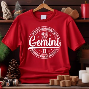 May include: Red t-shirt with a white circle graphic featuring the Gemini zodiac sign, the Roman numeral II, and the words "Intellectual-Friendly-Witty", "Gemini", "Adjustable-Versatile-Enthusiastic".