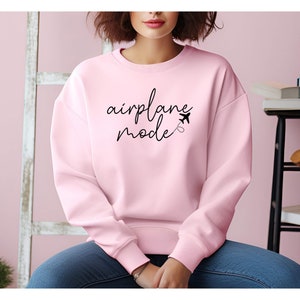 Puede incluir: Una sudadera rosa con el texto "airplane mode" en escritura negra con un peque&ntilde;o gr&aacute;fico de avi&oacute;n.