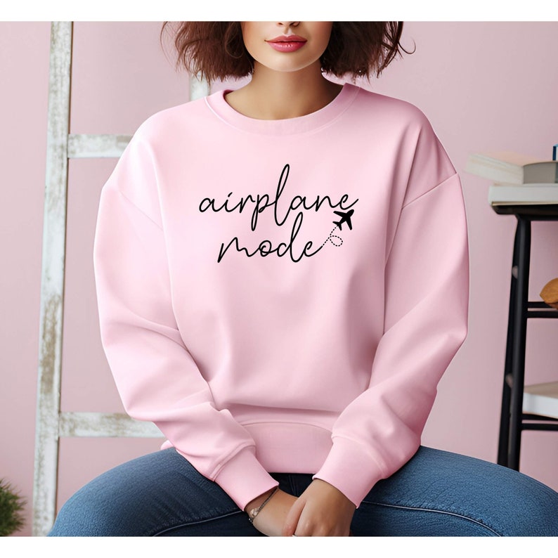 Puede incluir: Una sudadera rosa con el texto "airplane mode" en escritura negra con un peque&ntilde;o gr&aacute;fico de avi&oacute;n.