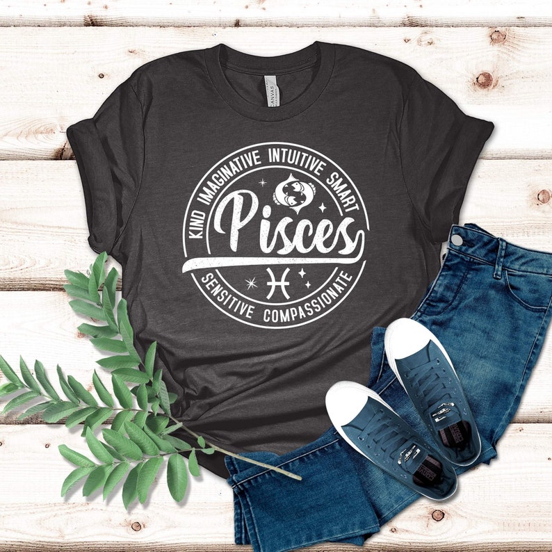 Może przedstawiać: Szary t-shirt z białym kołem z napisem "Ryby" z symbolem zodiaku Ryb i słowami "Miły, Wyobraźnia, Intuicja, Inteligentny, Wrażliwy, Wsp&oacute;łczujący".