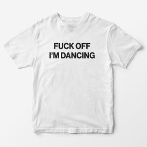 May include: A white t-shirt with the words "FUCK OFF I'M DANCING" printed in black. The text is centered on the front of the short-sleeved shirt. The background is a plain white surface.