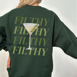 May include: Dark green sweatshirt featuring a graphic of a martini glass with olives and the word "FILTHY" repeated four times.