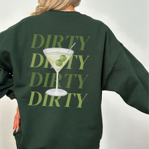 May include: A dark green sweatshirt with the text "DIRTY" repeated four times in a stacked pattern. A martini glass with two green olives is centered between the words.