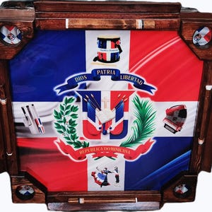 May include: A wooden domino table featuring the flag of the Dominican Republic. The table has a dark brown frame with inlaid cigar holders and decorative corner accents. The flag design includes the national coat of arms and the words "Dios, Patria, Libertad."