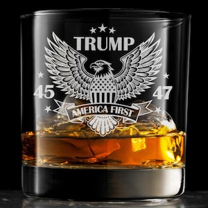 May include: A clear glass with an etched design of an eagle with wings spread, a banner reading "America First", and the numbers "45" and "47". The glass is filled with amber liquid and ice cubes.
