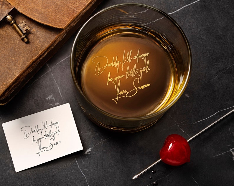 May include: A clear glass tumbler containing an amber liquid with the gold-etched text: Daddy, I'll always be your little girl. Love, Susan. A white card displays the same text in black script, alongside a red cherry on a silver metal cocktail pick.