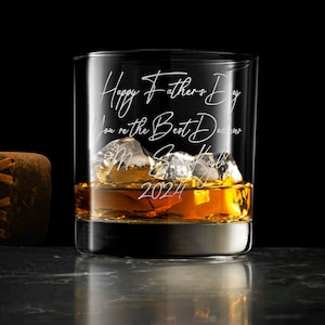 May include: A clear glass tumbler filled with amber liquid and ice cubes, featuring white engraved text that reads Happy Father's Day, You're the Best Dad ever, Love, Son, Kayla, 2024. A matching white card with the same text is visible.
