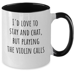 May include: White coffee mug with a black rim and handle. The mug has black text that reads "I'd love to stay and chat, but playing the violin calls."