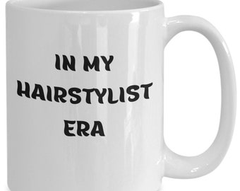 Może przedstawiać: Biały ceramiczny kubek do kawy z czarnym tekstem, który brzmi "In My Hair stylist Era".