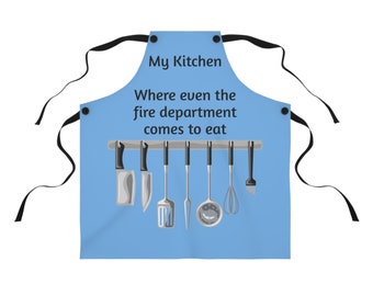 May include: A blue kitchen apron with the text "My Kitchen Where even the fire department comes to eat" and a row of kitchen utensils hanging on a rack.