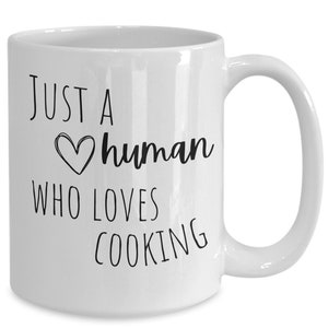 May include: White ceramic coffee mug with black text that reads "Just a human who loves cooking".