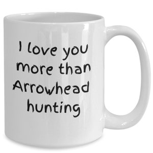 May include: White ceramic coffee mug with black text that reads "I love you more than arrowhead hunting".