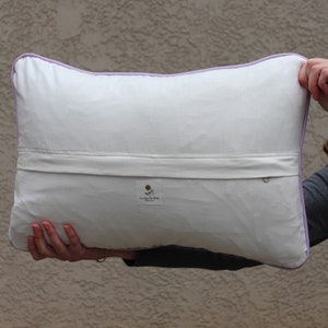 This shows the back of the pillow. The fabric is white, and there is a horizontal flap that runs the whole pillow to cover the zipper. In the center is a tag that states my business name.